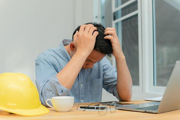 A man is sitting at a desk with his hands on his head.
