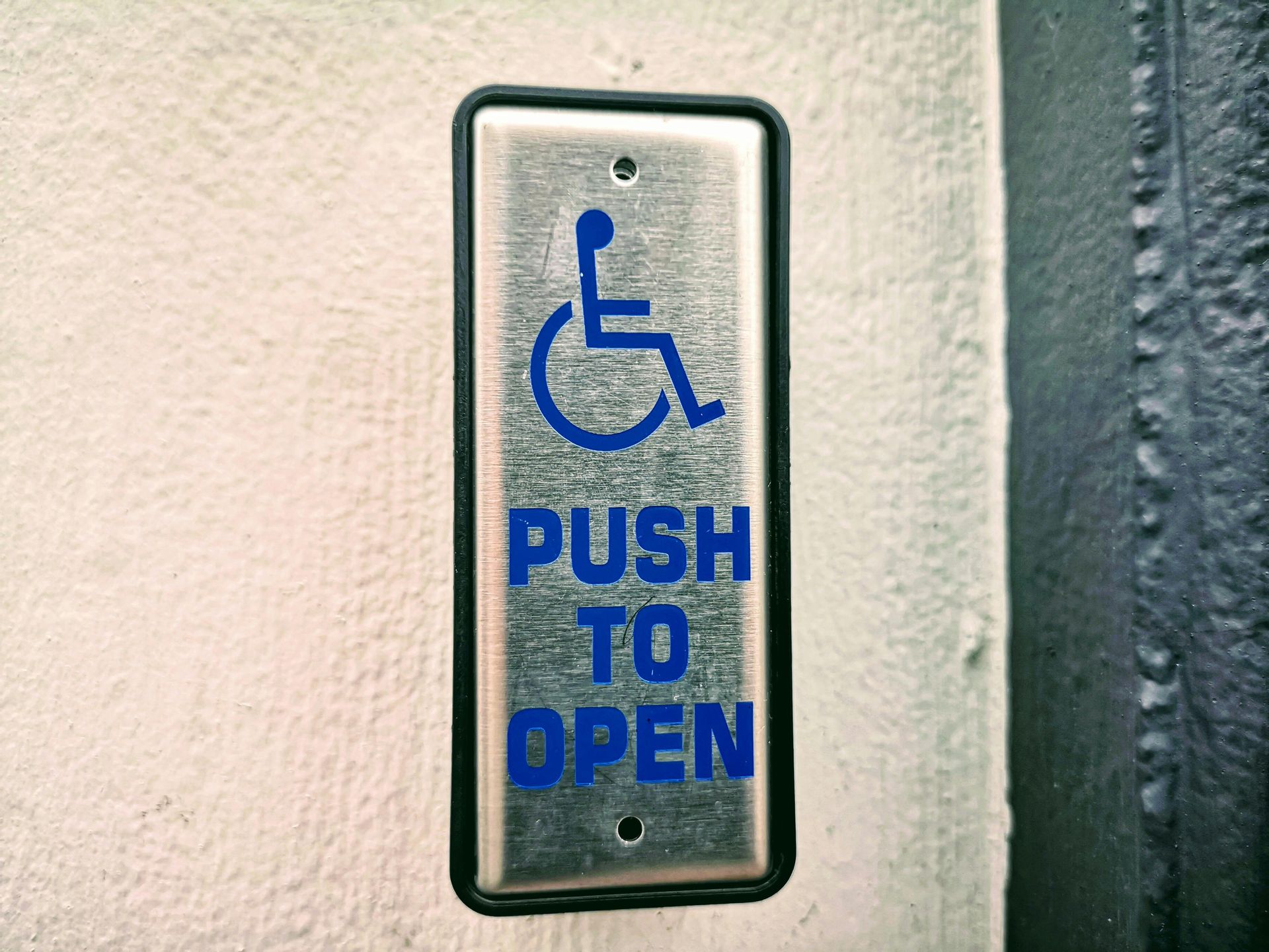 Blue wheelchair-accessible push-to-open sign on a wall-mounted door button panel