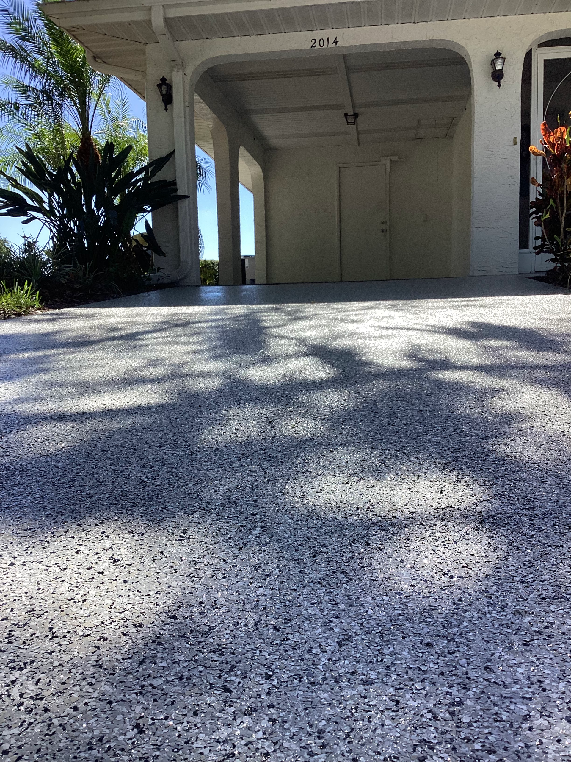A driveway leading to a garage with a white house in the background.