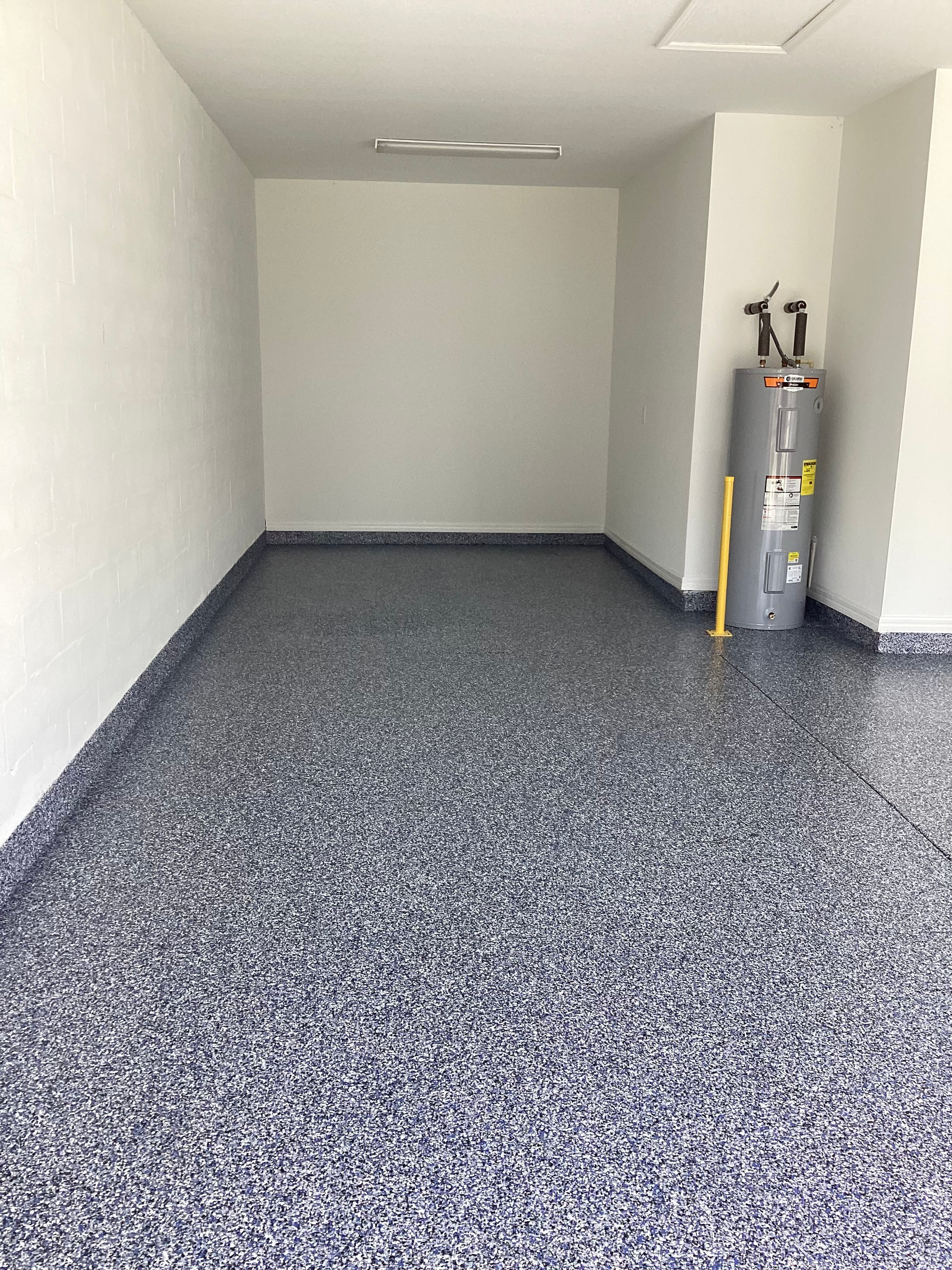 An empty garage with a water heater and a mop on the floor.