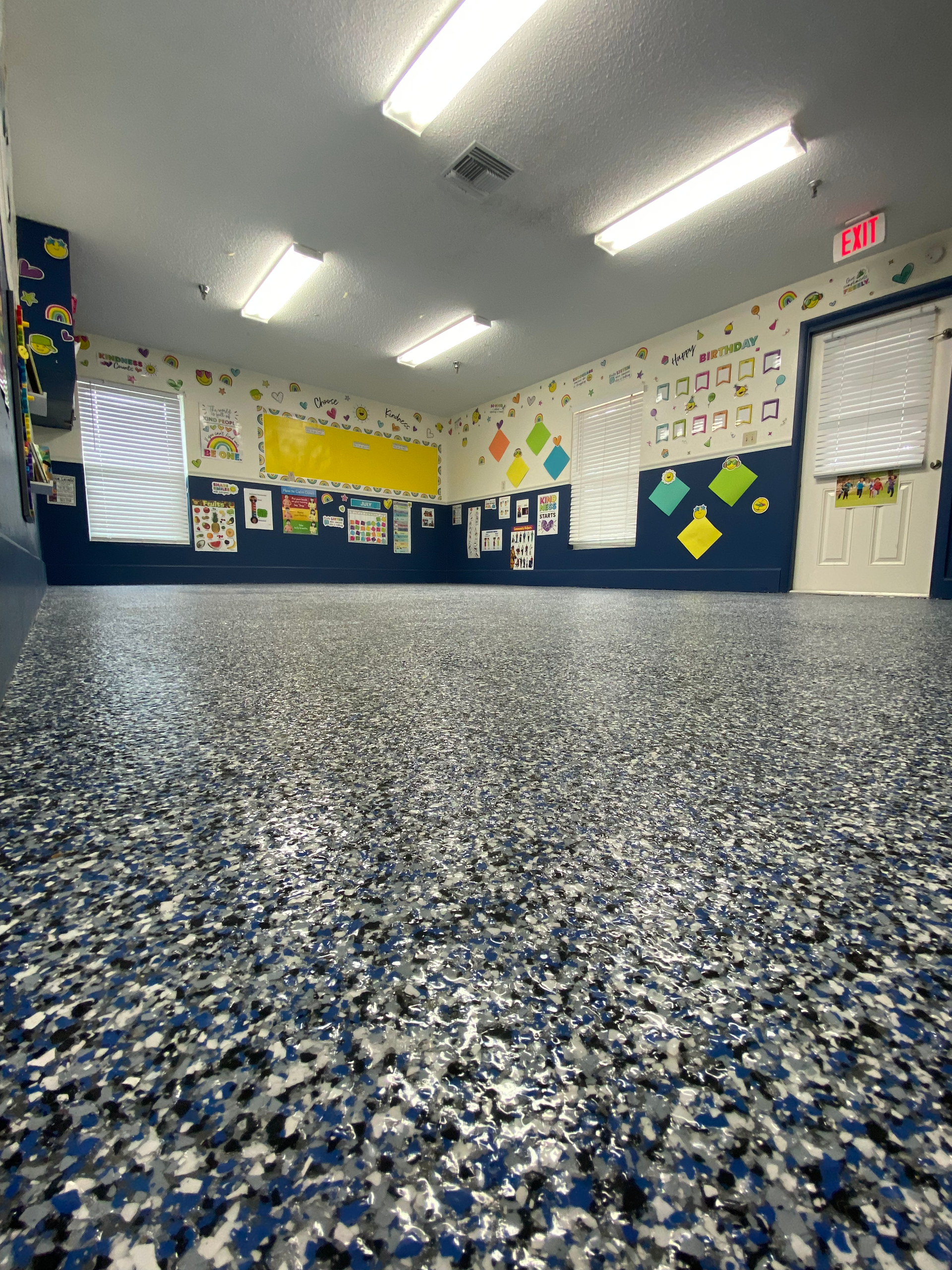 A large room with a gray and blue floor and a classroom in the background.