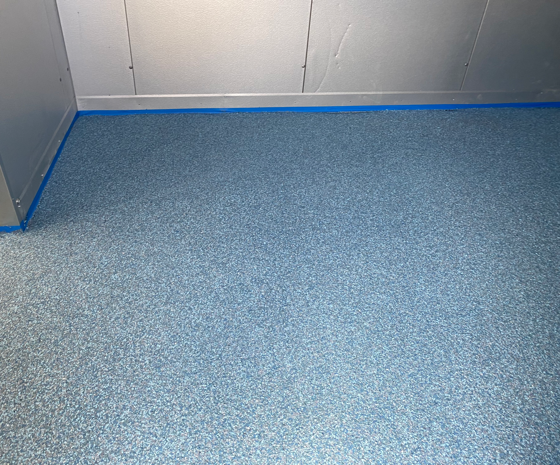 A blue carpeted floor in a room with blue tape on it.
