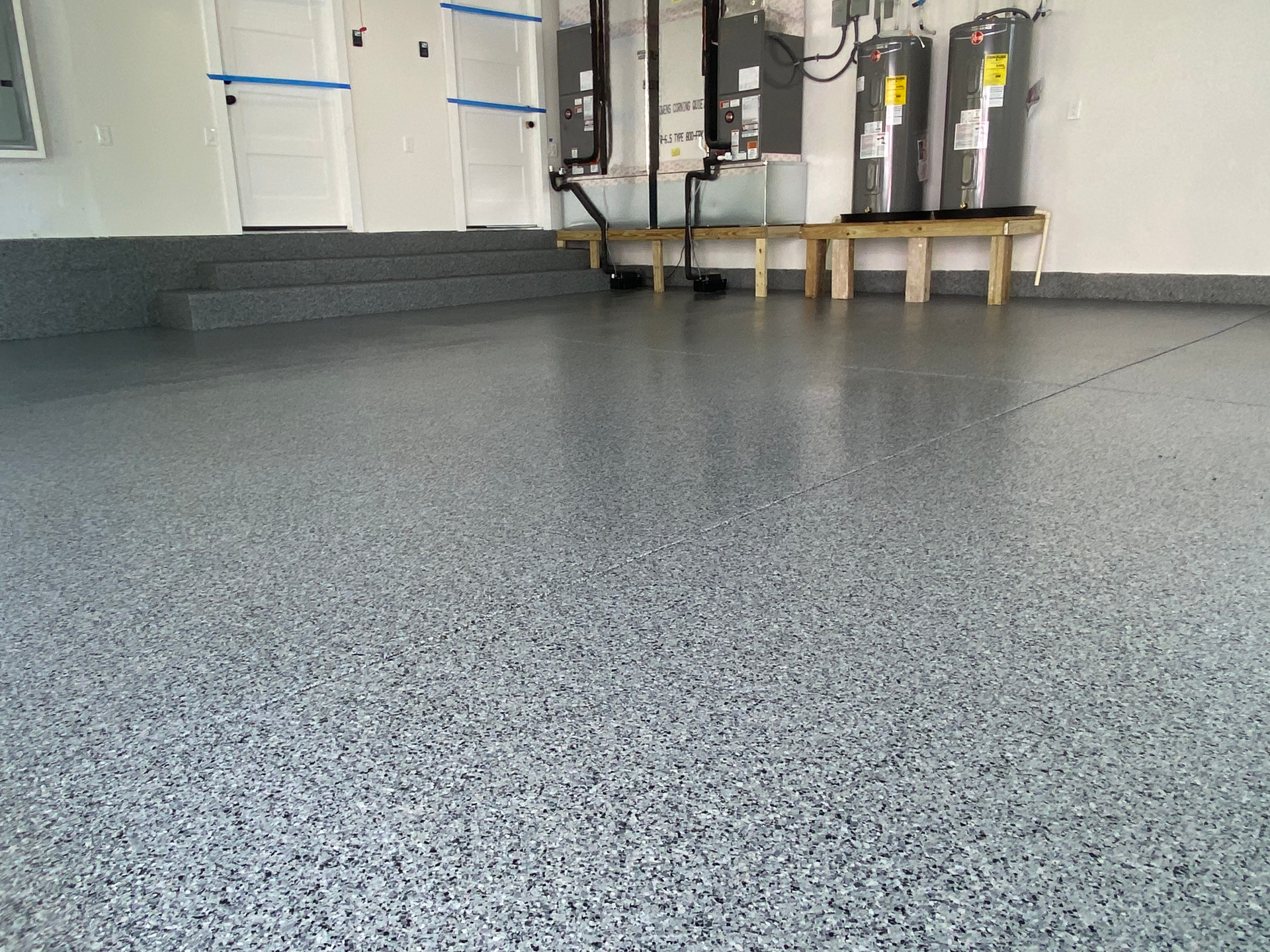 A garage with a gray floor and a row of water heaters.