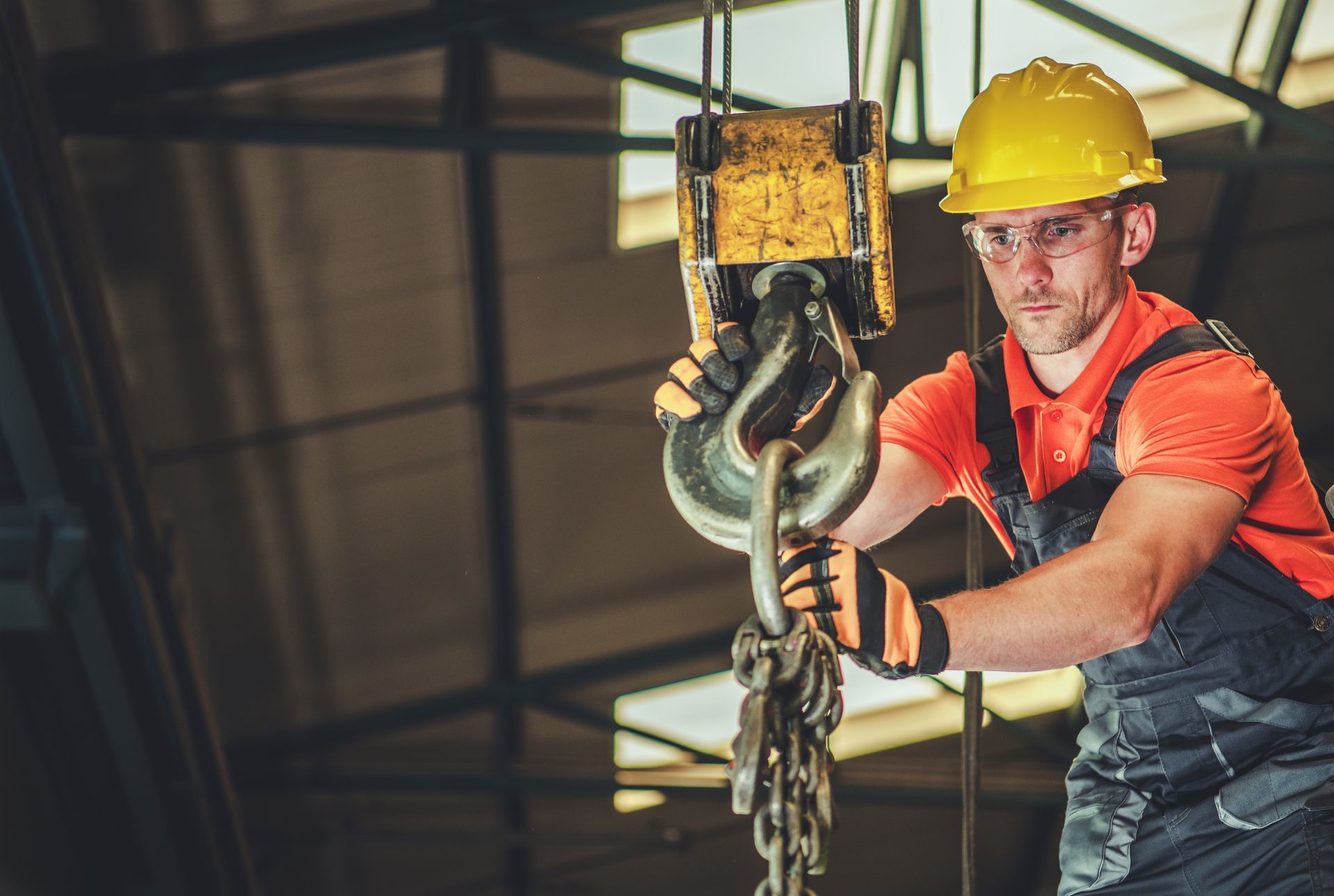 A construction worker is lifting a crane hook in a factory.