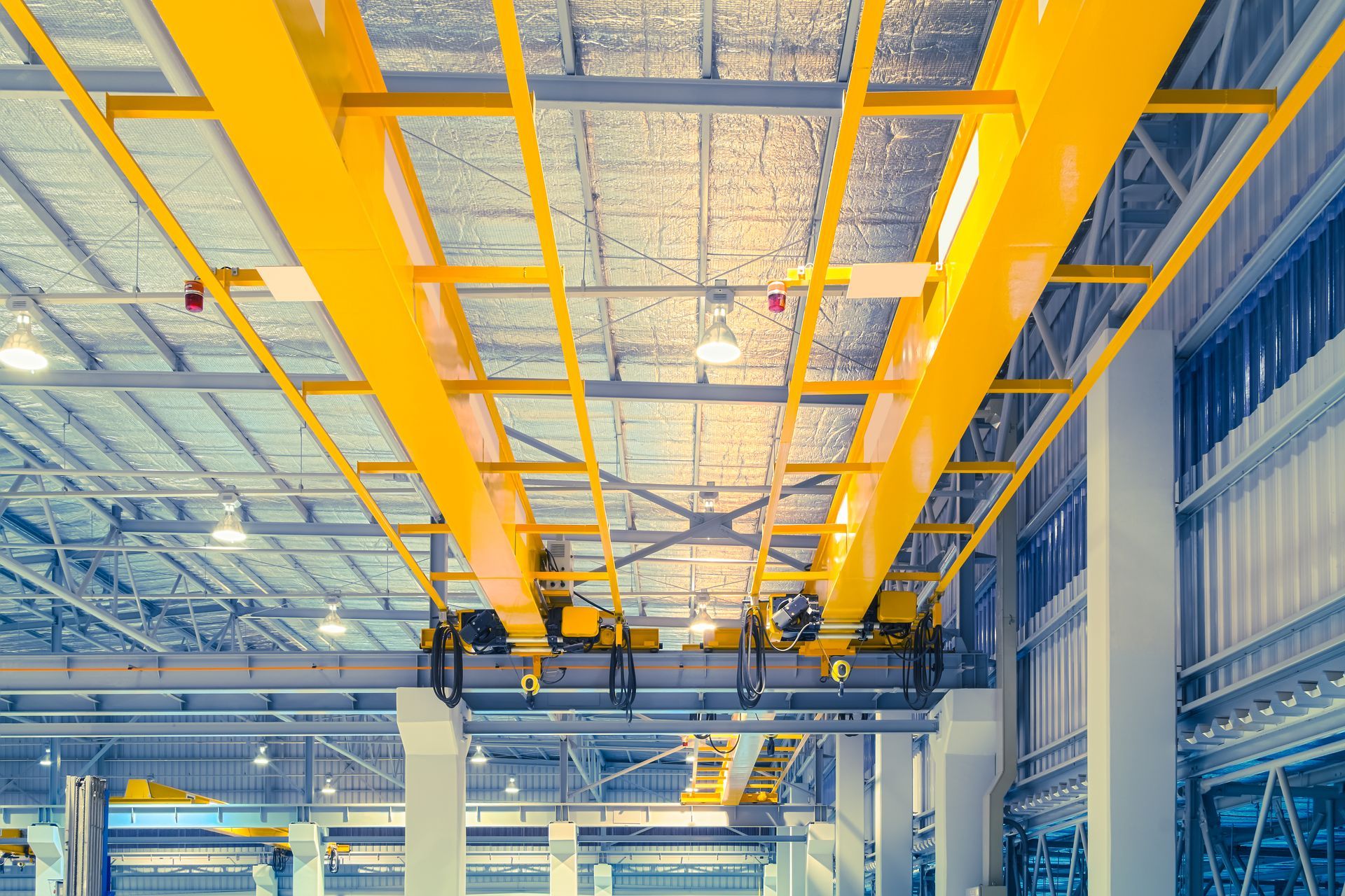 A large yellow crane is hanging from the ceiling of a factory.