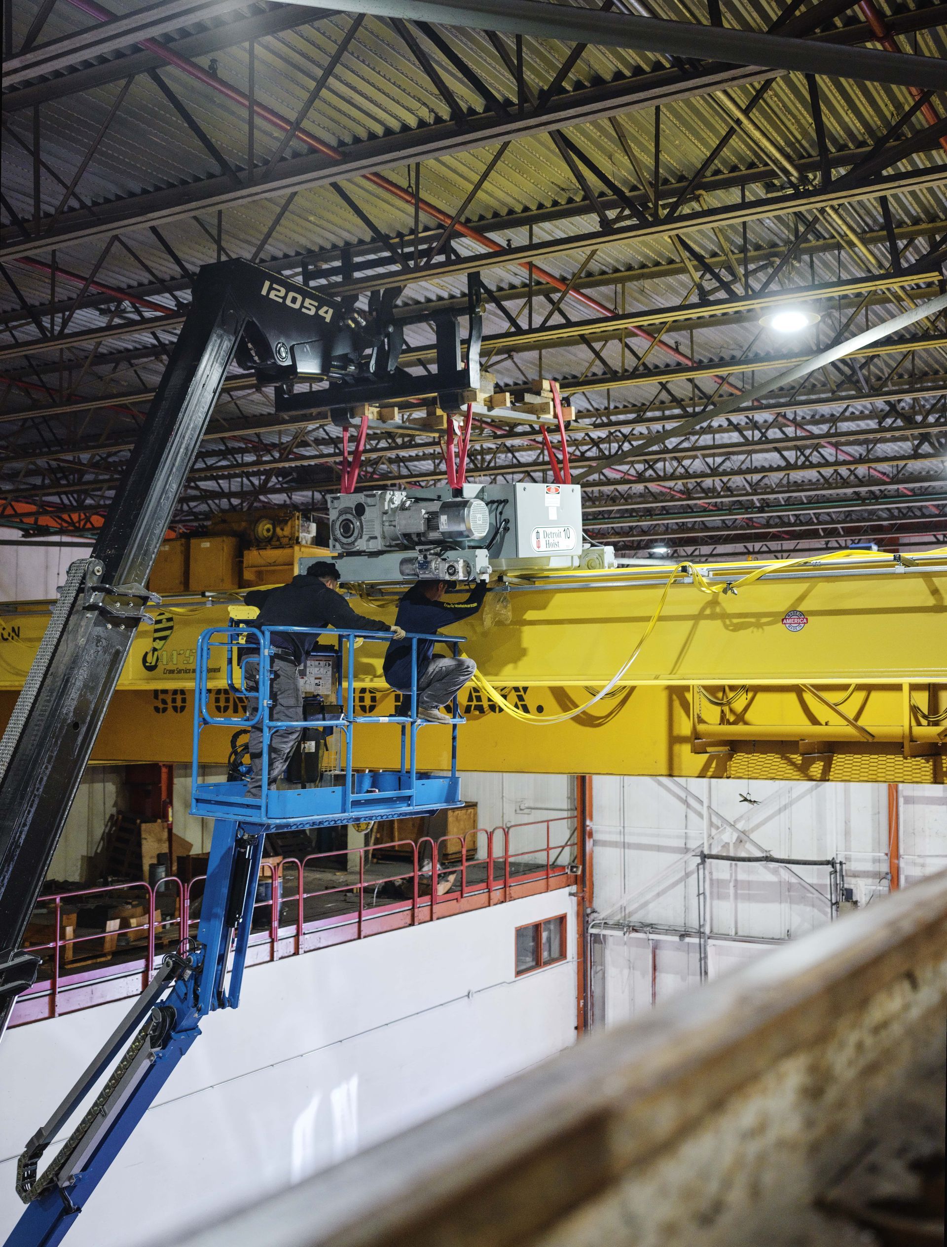 Two men are working on a crane in a warehouse