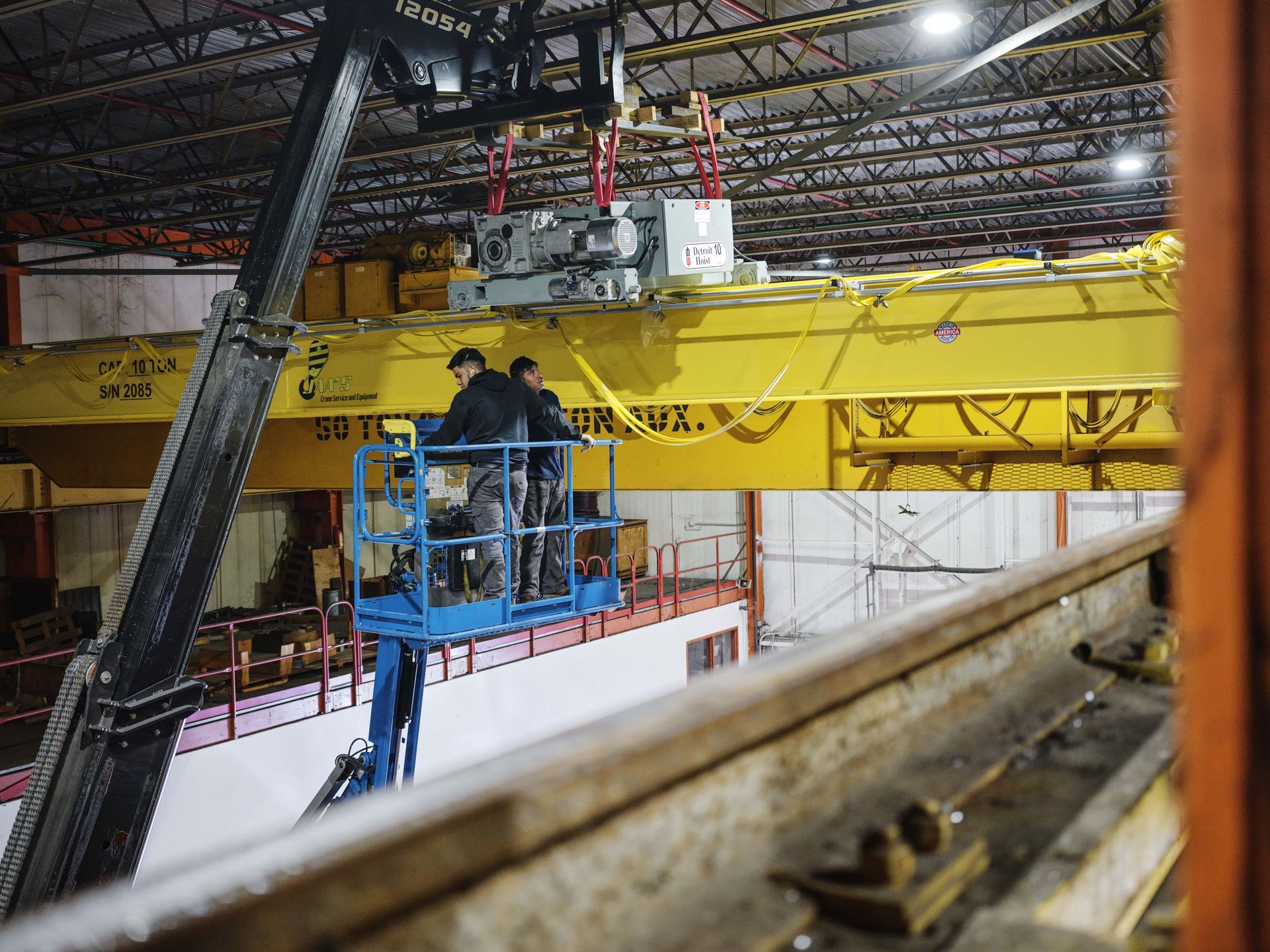 Two men are working on a crane in a factory.