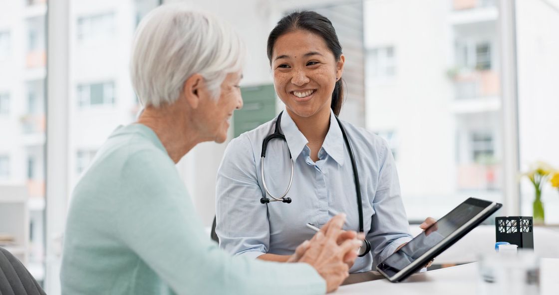 Der Arzt lächelt während einer Sprechstunde an einem Empfangstresen mit einem älteren Patienten.