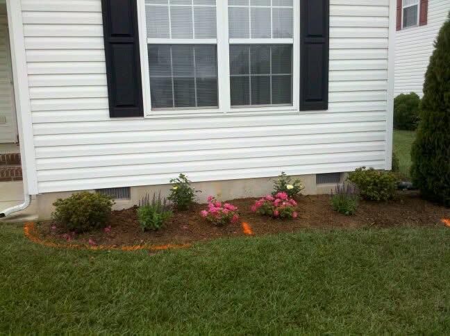 Front of house with black shutters and a small flower bed of pink blooms by the window.