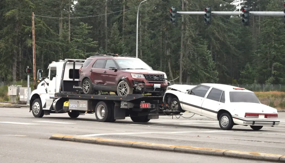 Tow truck hauling a maroon SUV after a white sedan crash on a roadside barrier