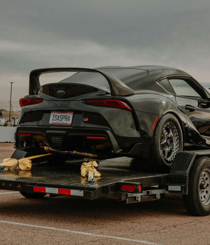 Black sports car strapped on a flatbed trailer under a cloudy sky