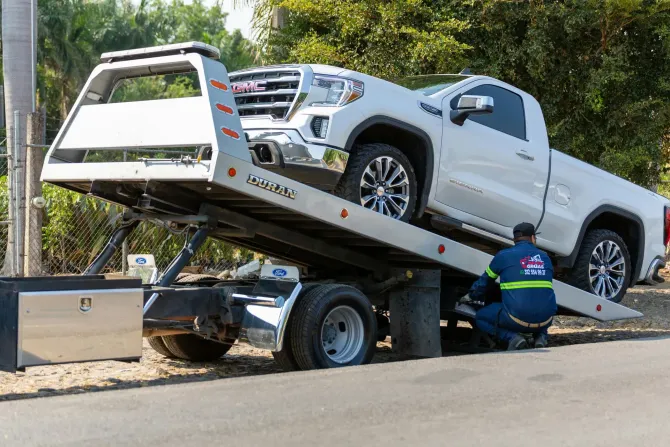 Tow truck loading a white pickup truck onto a flatbed trailer on a roadside