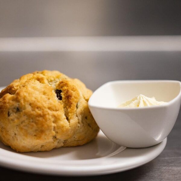 A golden-brown scone sits on a white plate next to a small bowl of clotted cream.