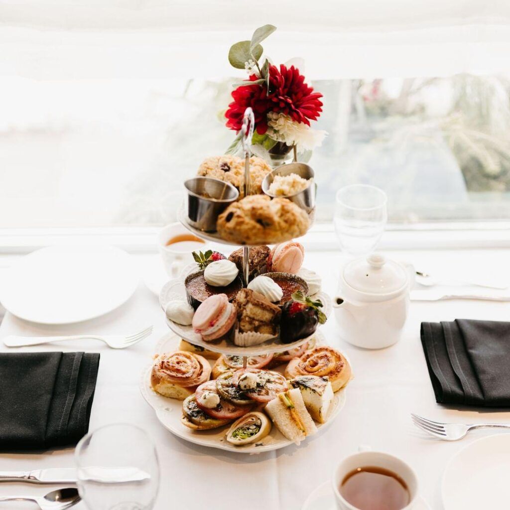 Tiered brunch stand with pastries and macarons on a bright table, topped with red flowers