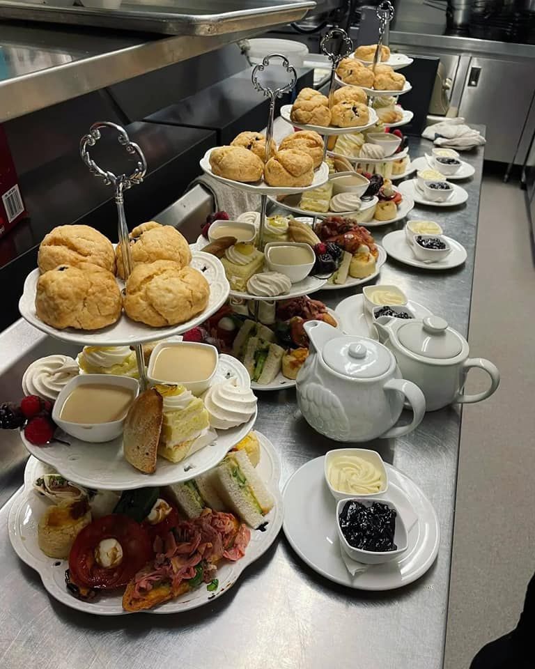 Tiered serving stands hold scones, sandwiches, and desserts on a stainless steel commercial kitchen counter.