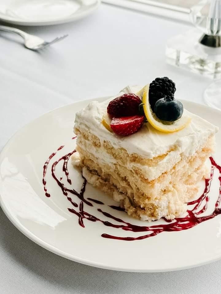 A small, layered strawberry shortcake topped with cream and fruit, resting on a white plate with a blueberry.
