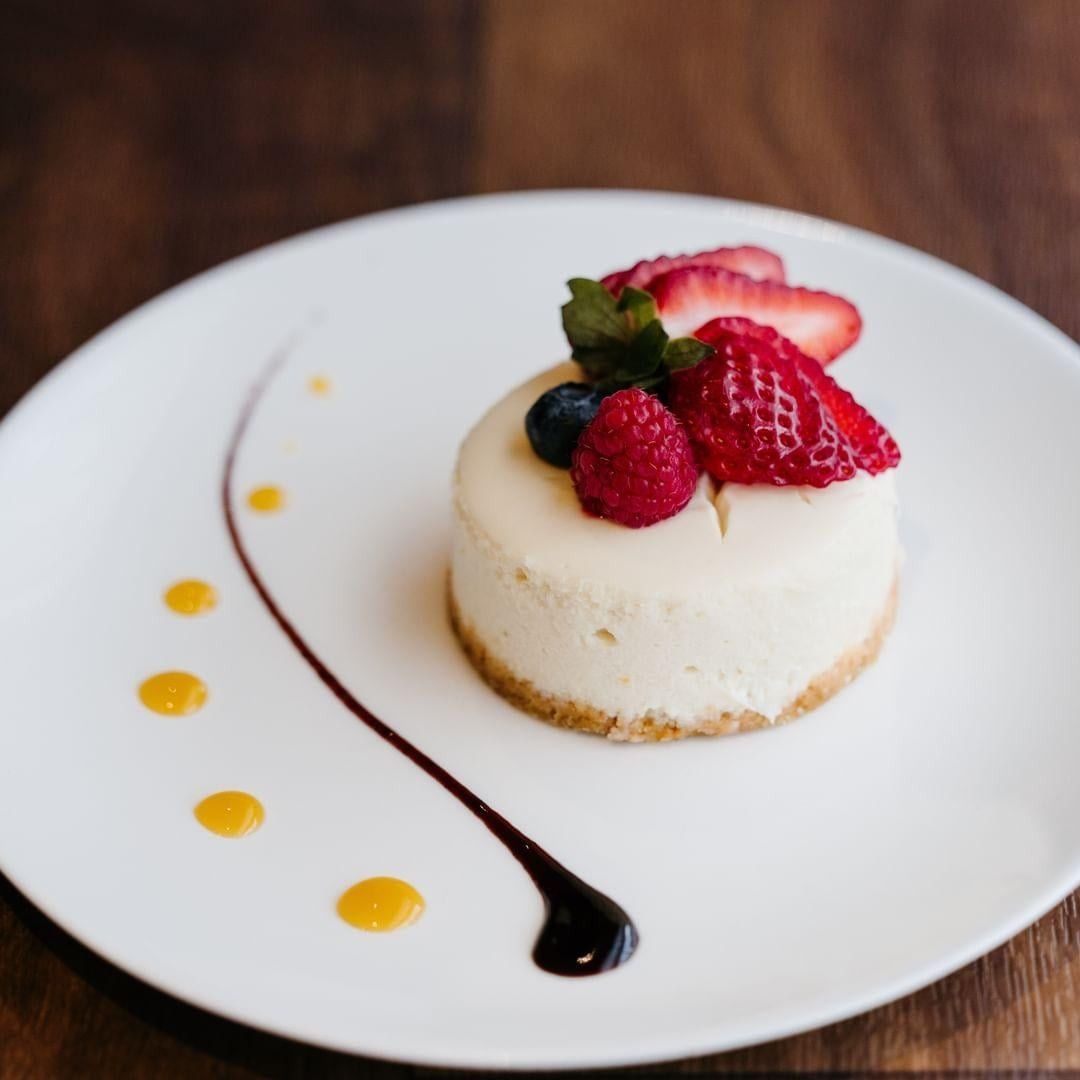 Small cheesecake topped with berries on a white plate with chocolate and caramel sauce drizzles