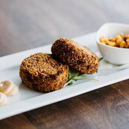 Breaded croquettes on a white platter with garnish and a small dipping bowl on a wooden table