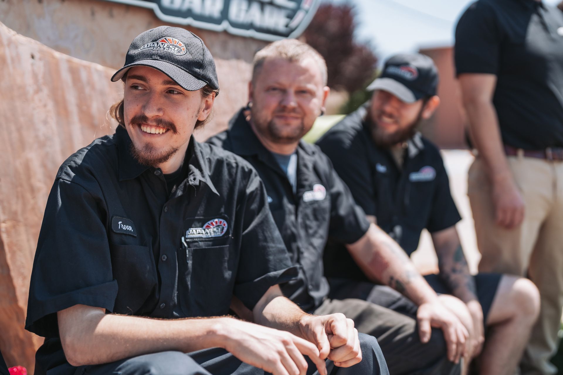 A group of men are sitting next to each other in front of a sign. | Japanese Car Care