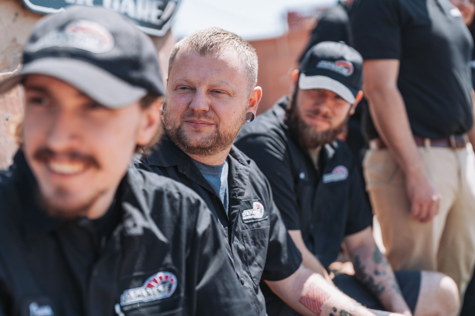 A group of men are sitting in a row wearing black shirts and hats. | Japanese Car Care