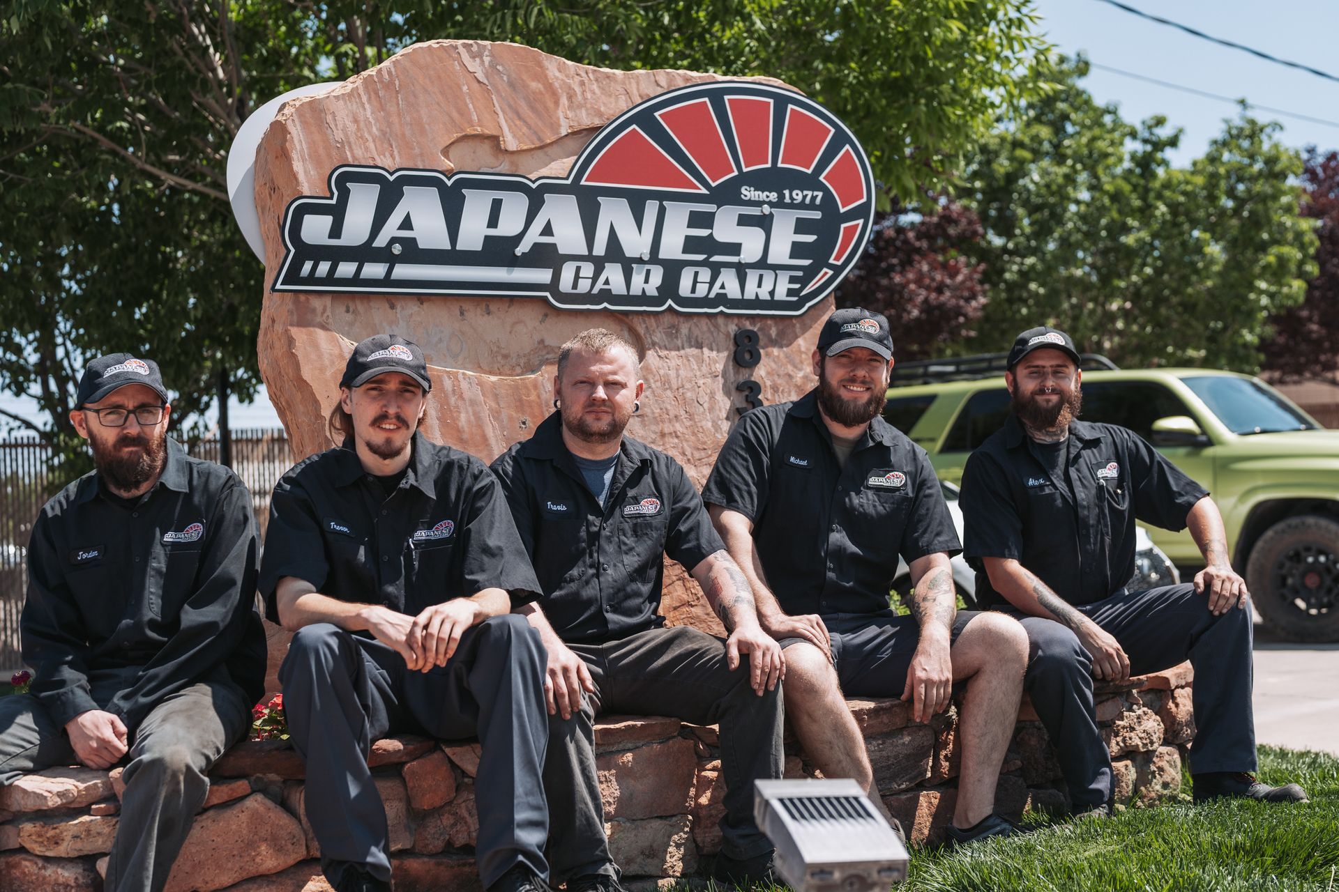 A group of men are sitting in front of a japanese sign | Japanese Car Care