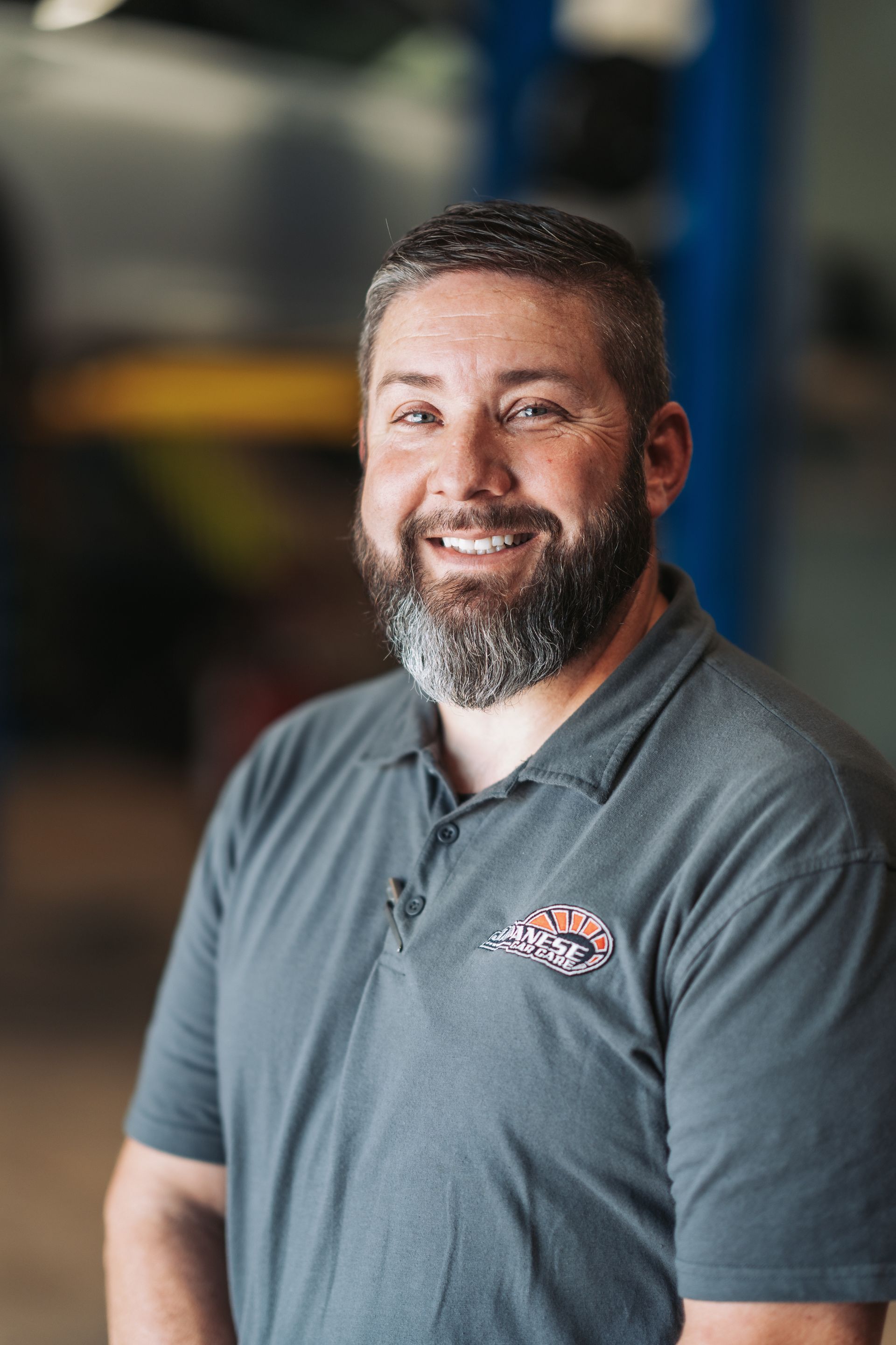 A man with a beard is smiling for the camera in a garage. | Japanese Car Care
