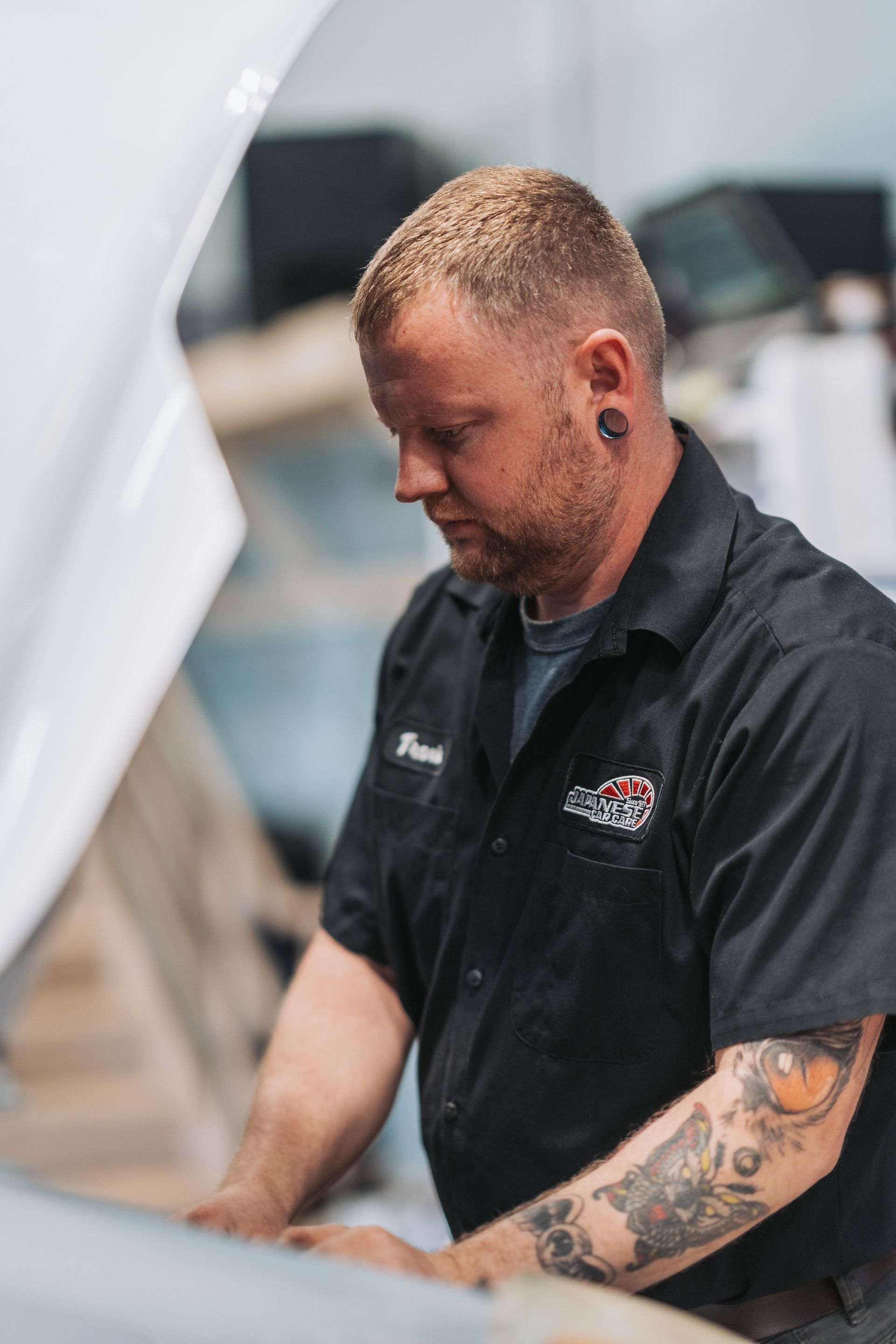 A man with tattoos is working on a car with the hood open. | Japanese Car Care