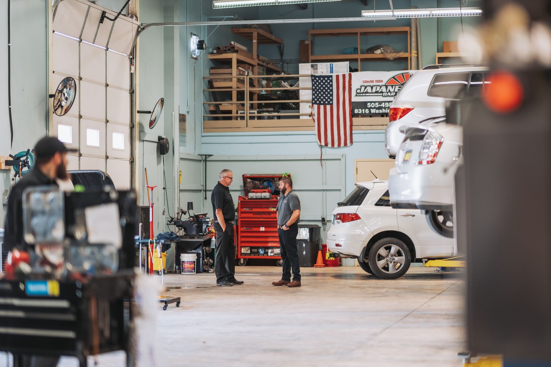 Two men are standing in a garage next to a car. | Japanese Car Care
