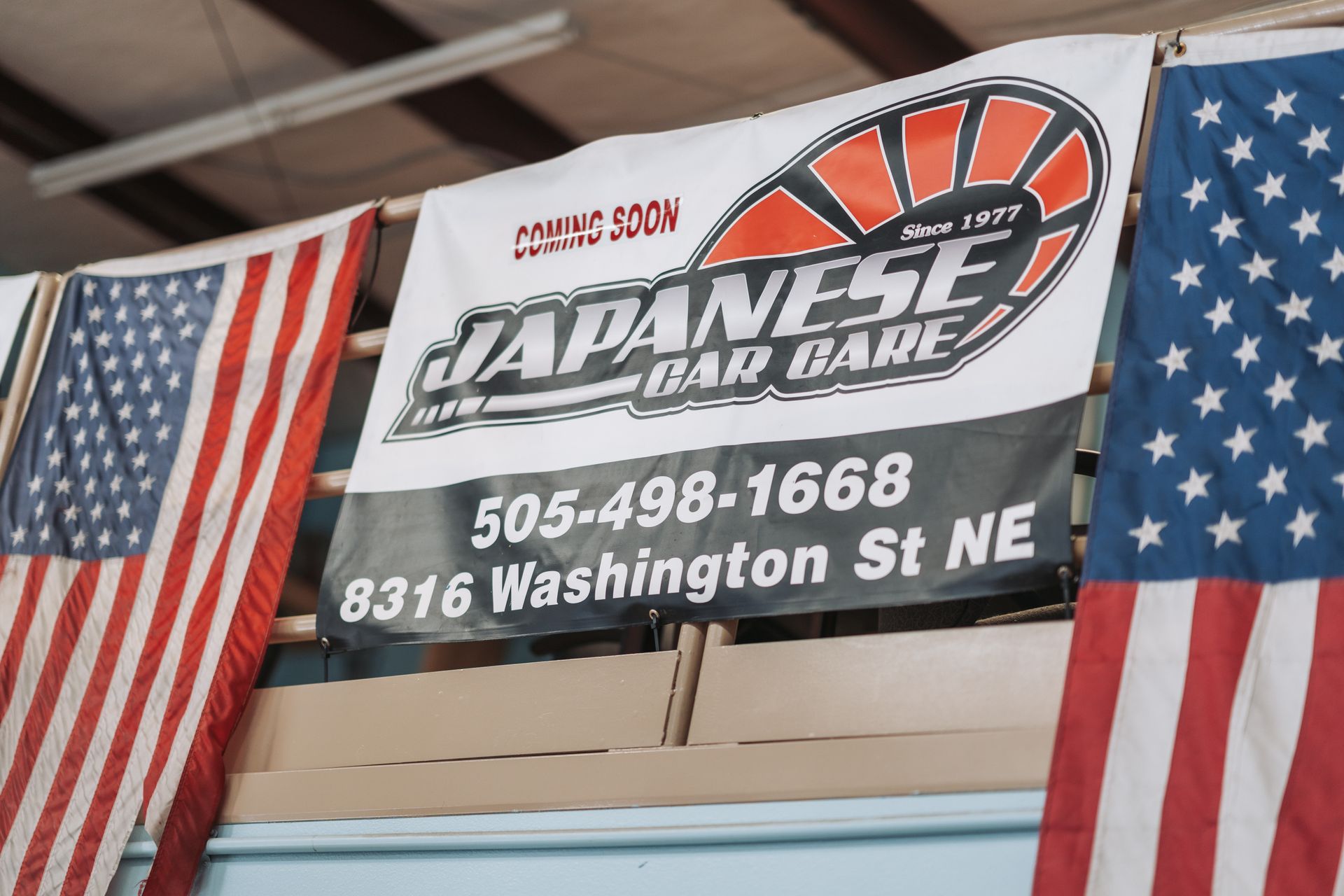 A banner for japanese car care hangs between two american flags | Japanese Car Care