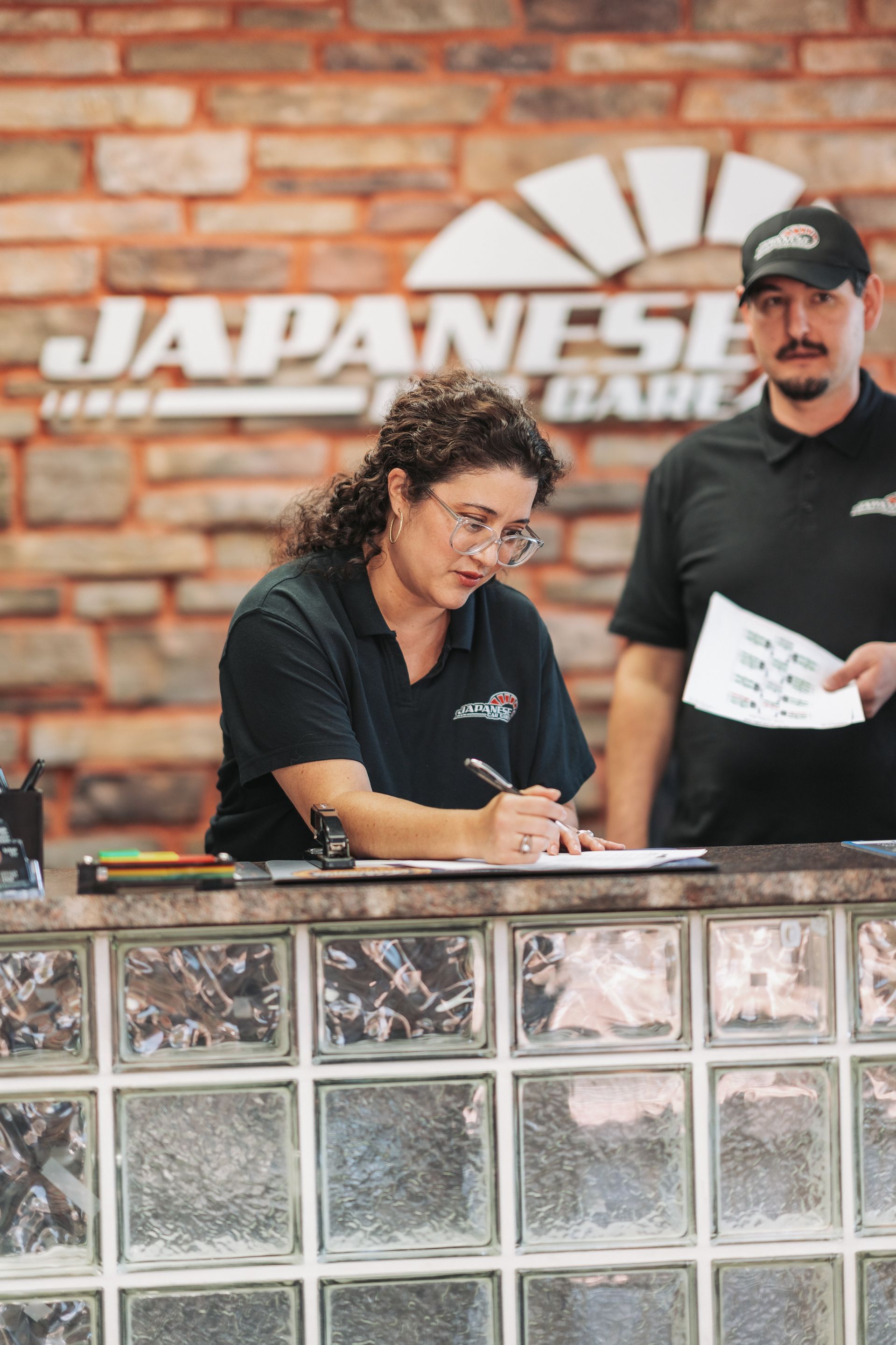 A man and a woman are standing behind a counter at a japanese auto repair shop. | Japanese Car Care