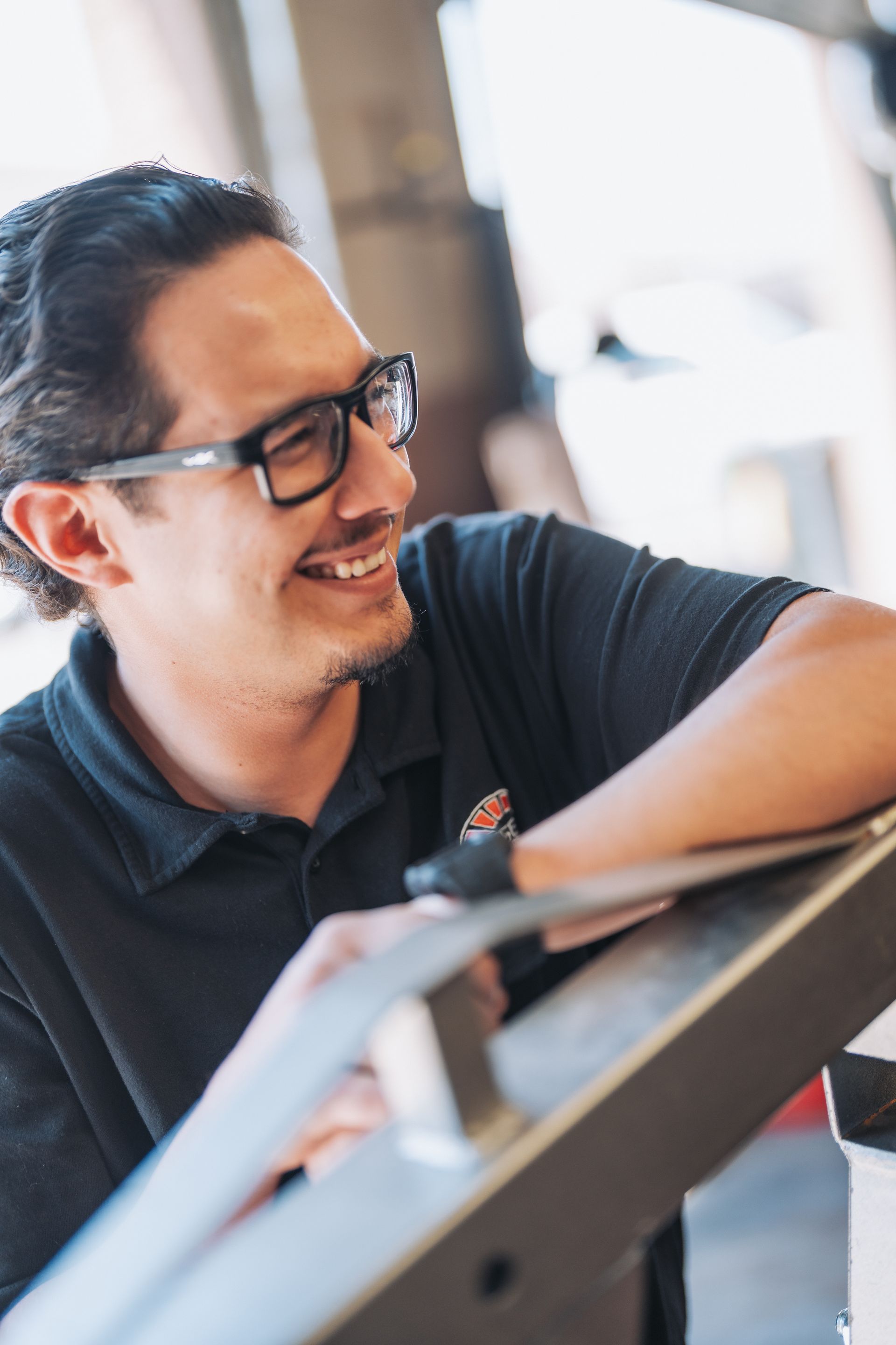 A man wearing glasses is smiling while leaning on a table. | Japanese Car Care