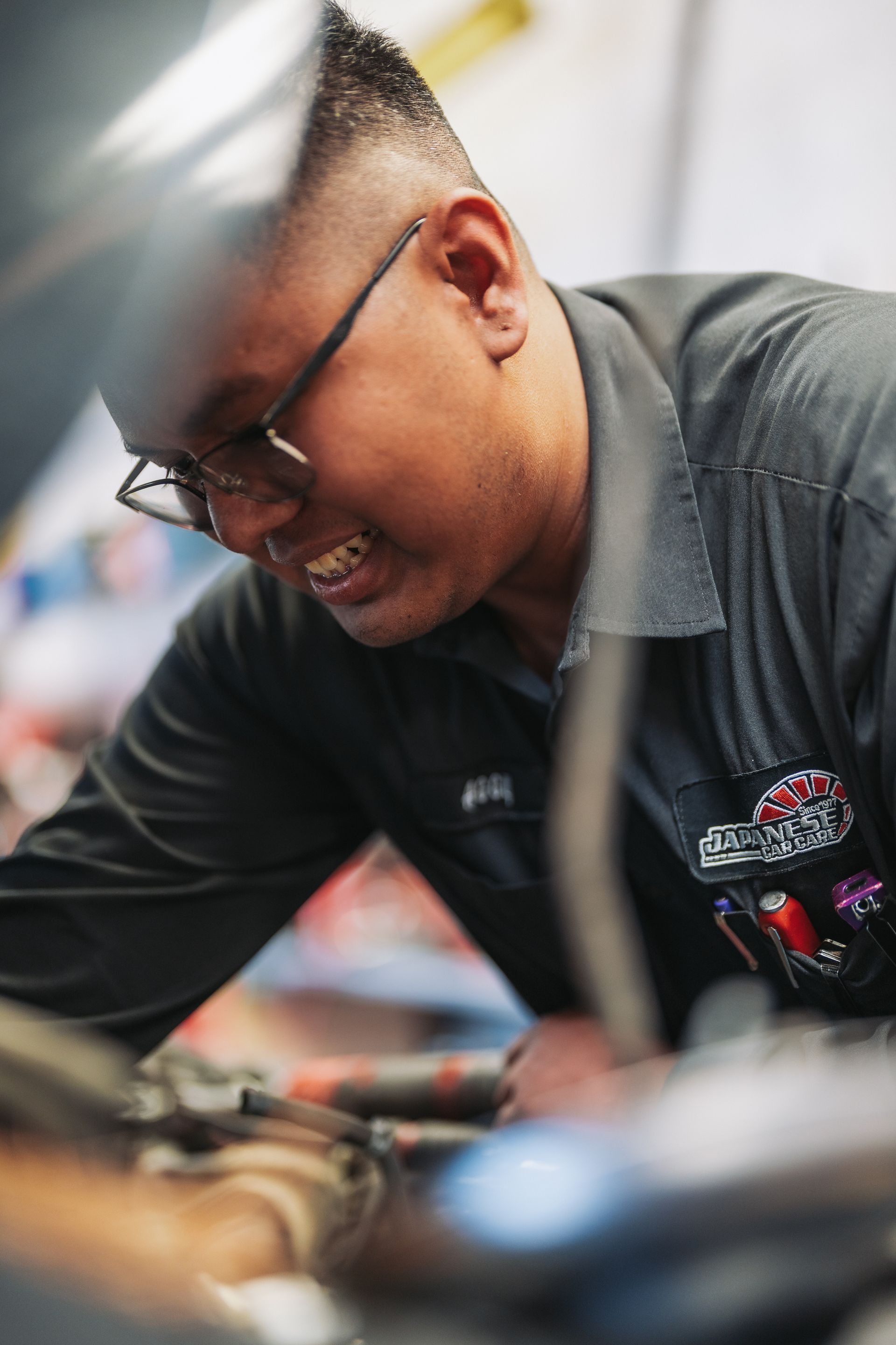A man wearing glasses is working on a car engine. | Japanese Car Care