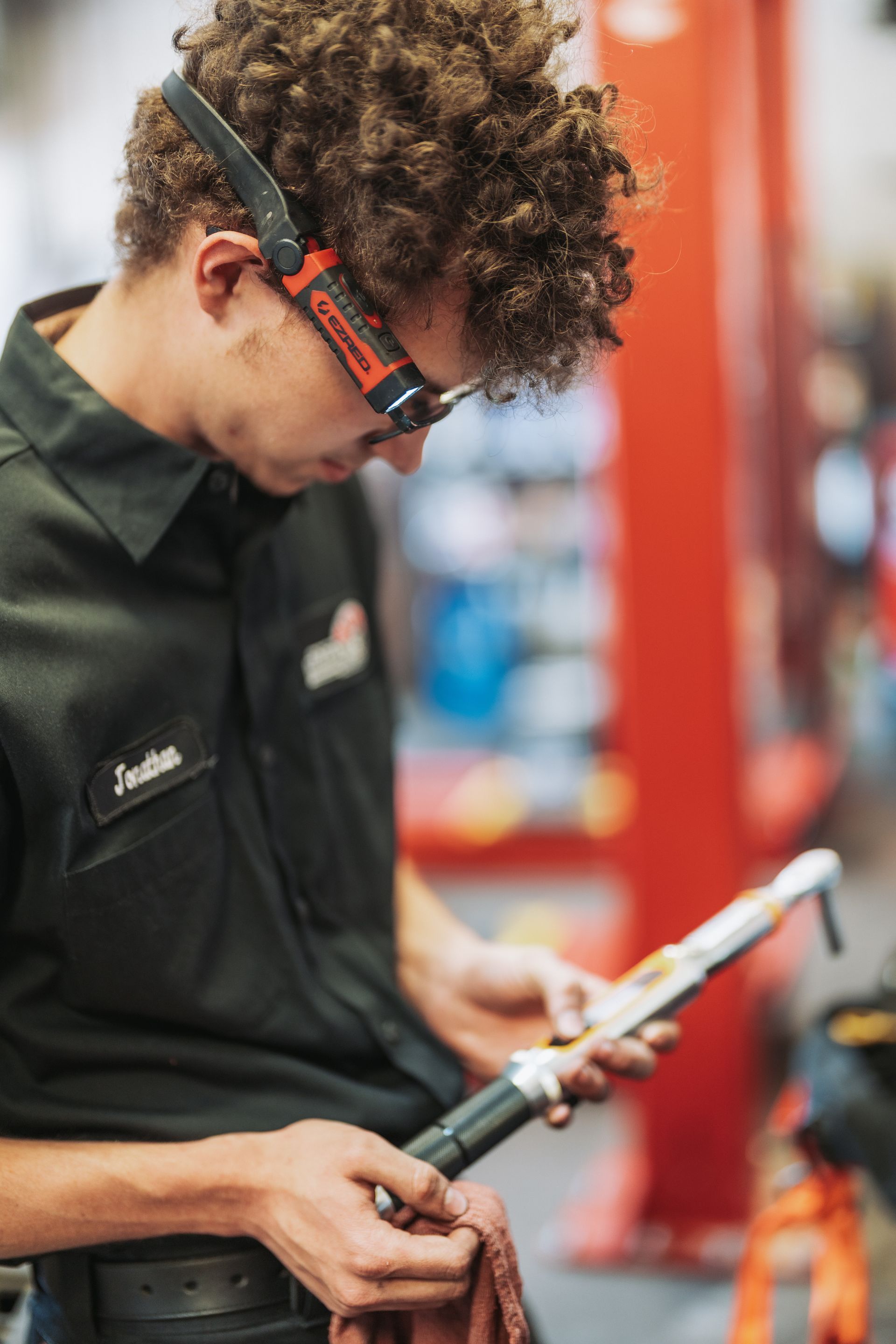 A young man wearing a headlamp is working on a bicycle in a garage. | Japanese Car Care