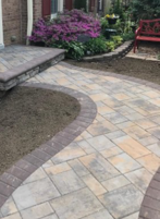 Curved stone patio walkway beside garden beds, with a red bench and steps leading to a house.