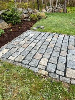 Cobblestone patio beside grass and a rock garden in a backyard