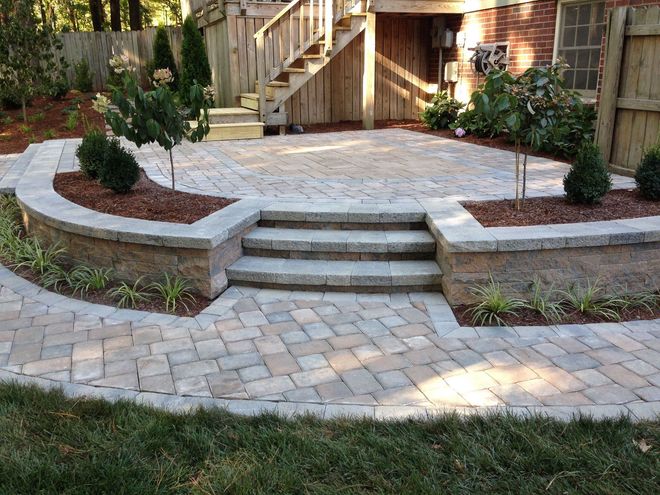 Stone patio with curved steps, paver walkway, and raised garden beds in a backyard