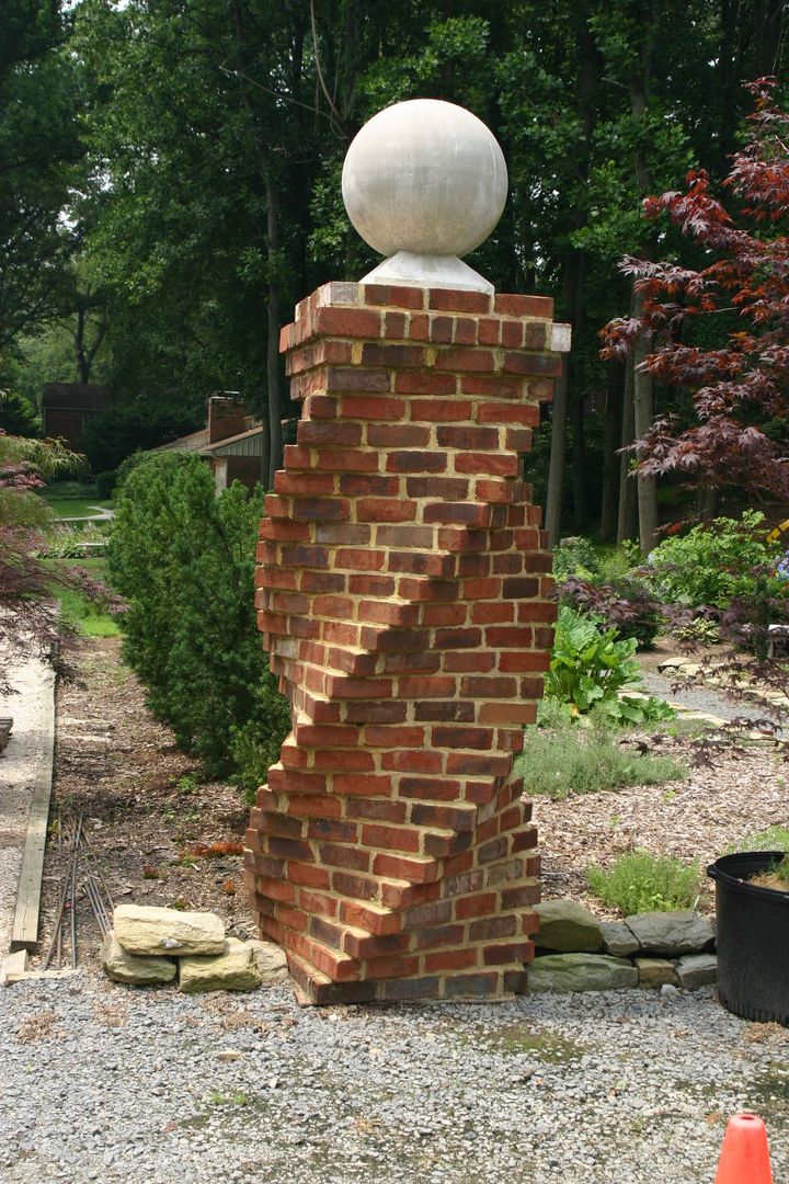 A decorative red brick pillar with a twisted design, topped with a stone sphere, standing in a landscaped garden.