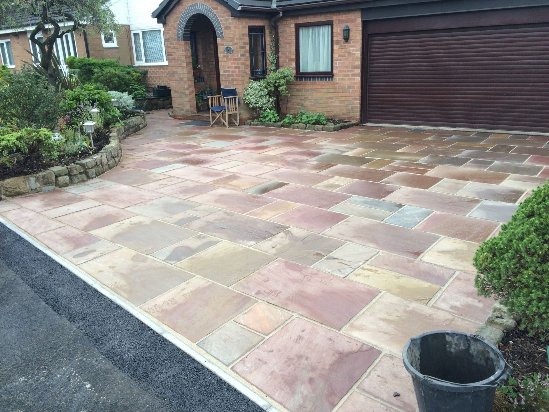 Front driveway with multicolored paving stones, brick house, garage door, and a small garden border.