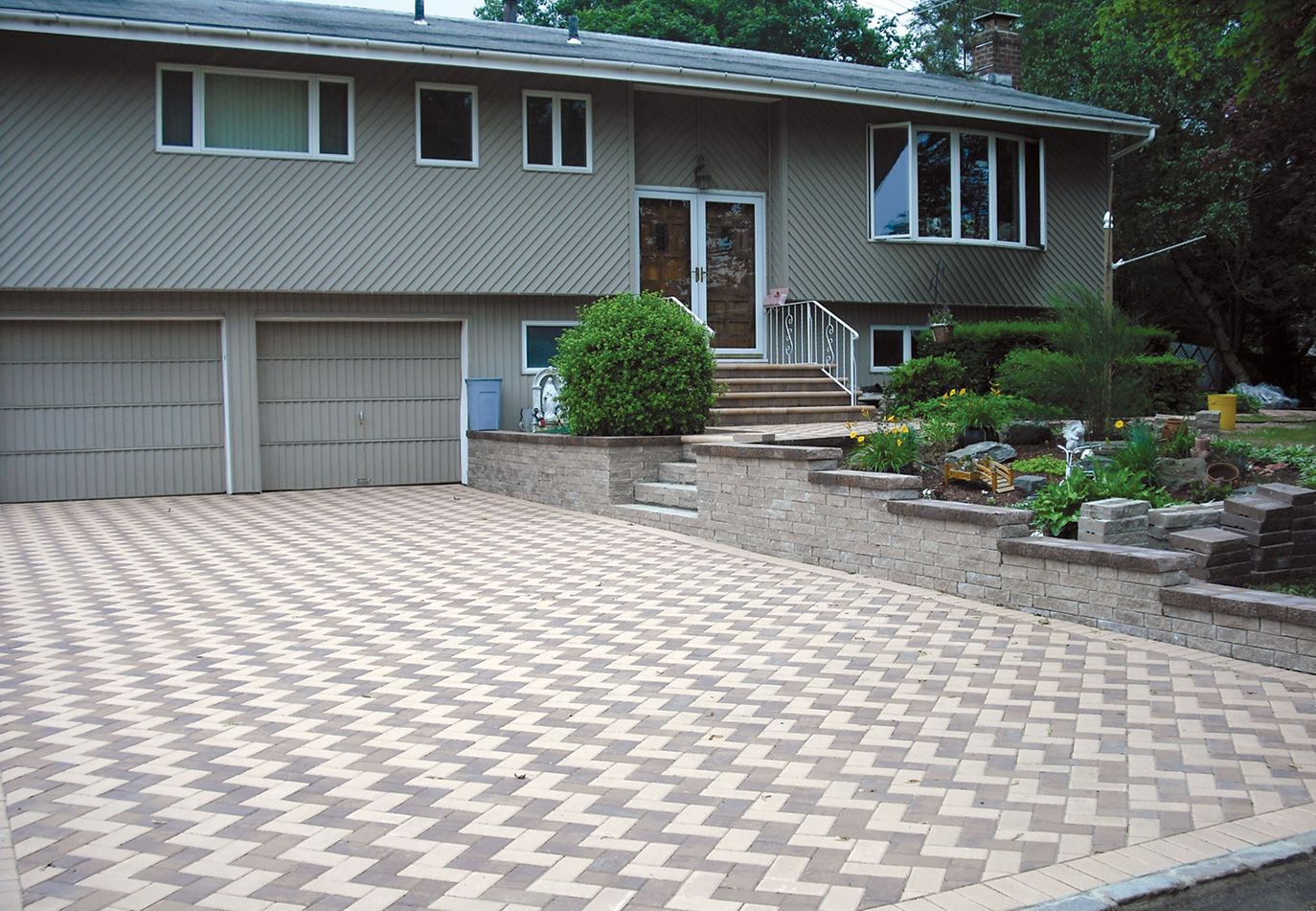 Paver driveway leading to a suburban house with two garage doors and a landscaped front entrance
