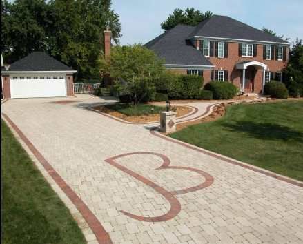 Brick driveway with a large decorative red pattern leading to a brick house and detached garage