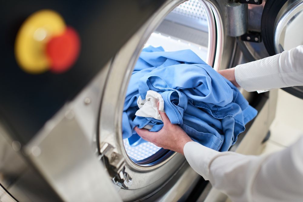 A Person is Putting a Shirt in a Washing Machine — Super Suds Commercial Laundry in Avoca, QLD