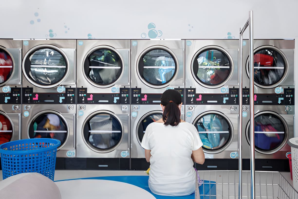 A Woman is Sitting in Front of a Row of Washing Machine — Super Suds Laundry in Avoca, QLD
