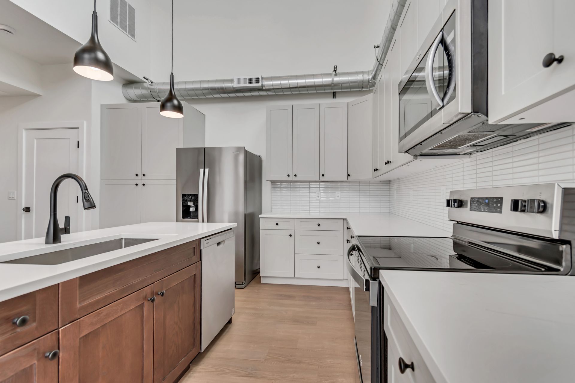 Modern kitchen with white and brown cabinets, stainless steel appliances, and overhead lighting.