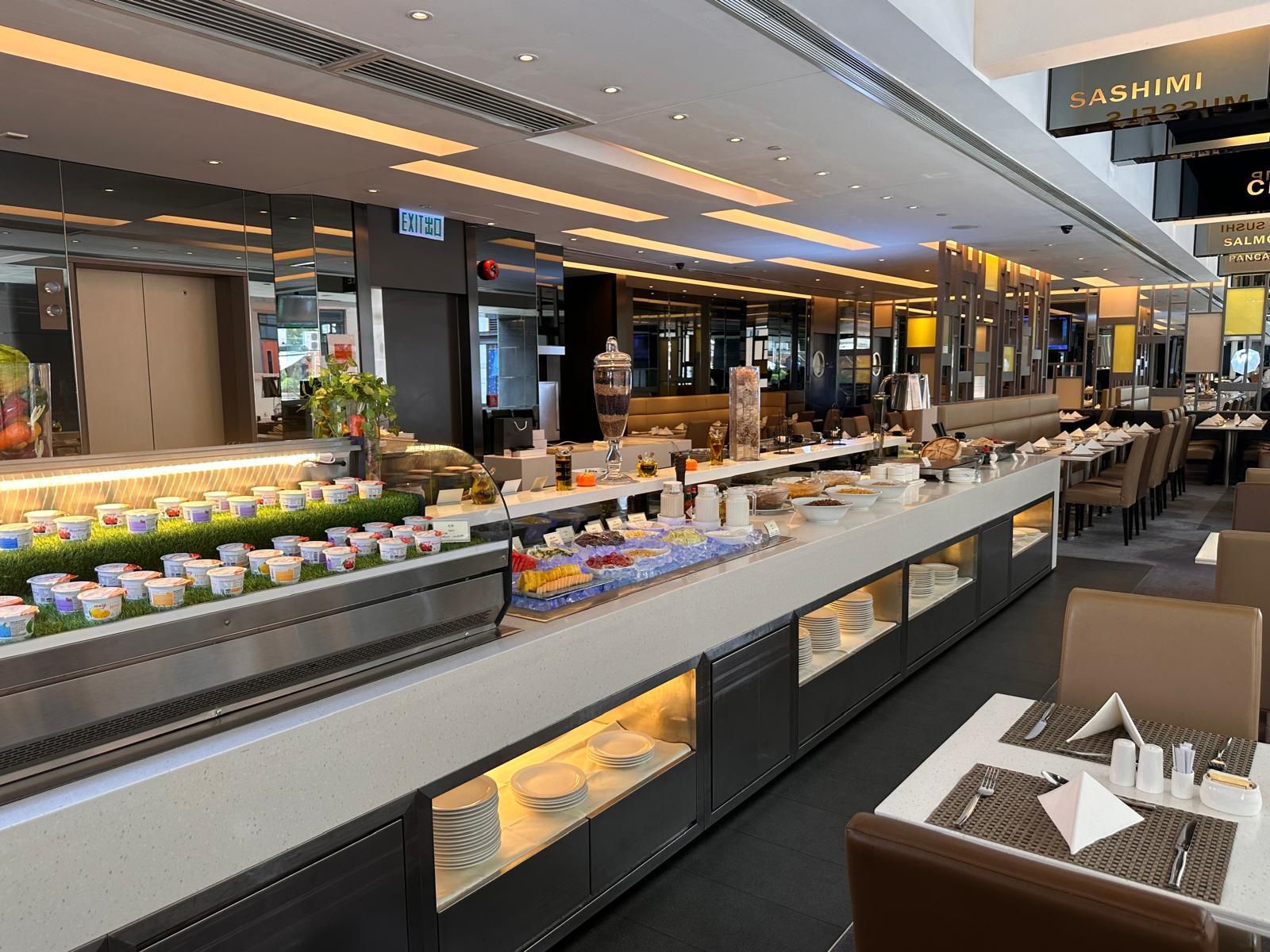 Buffet with various food displays. Restaurant setting. White counters, tables, and chairs.