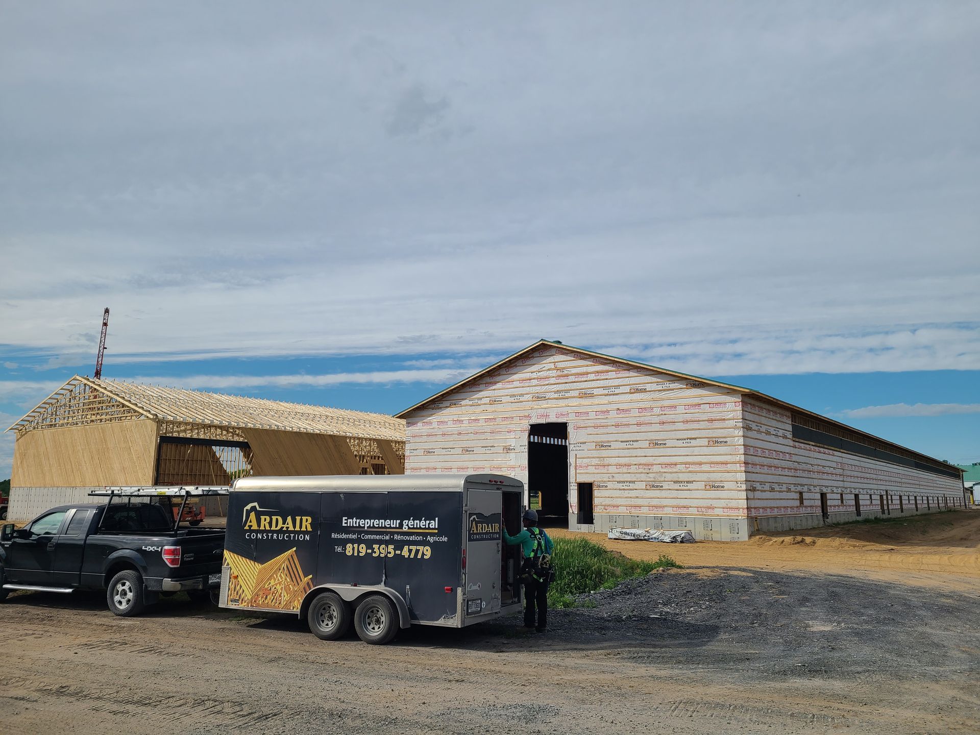 Un camion noir avec une remorque est stationné sur un chantier de construction où se trouvent deux grands bâtiments partiellement achevés.