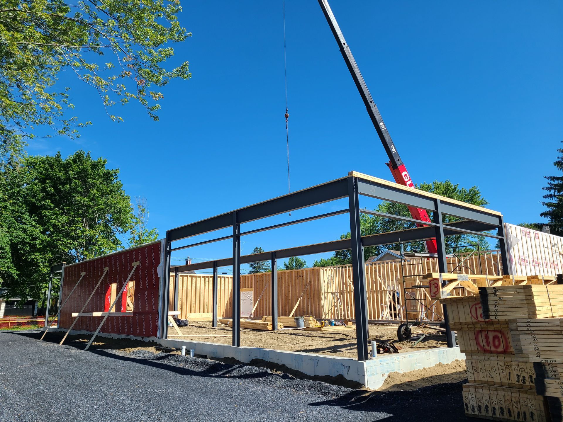 Un chantier de construction montrant une structure à ossature métallique en cours d'édification, avec une grue visible sur un ciel bleu dégagé.