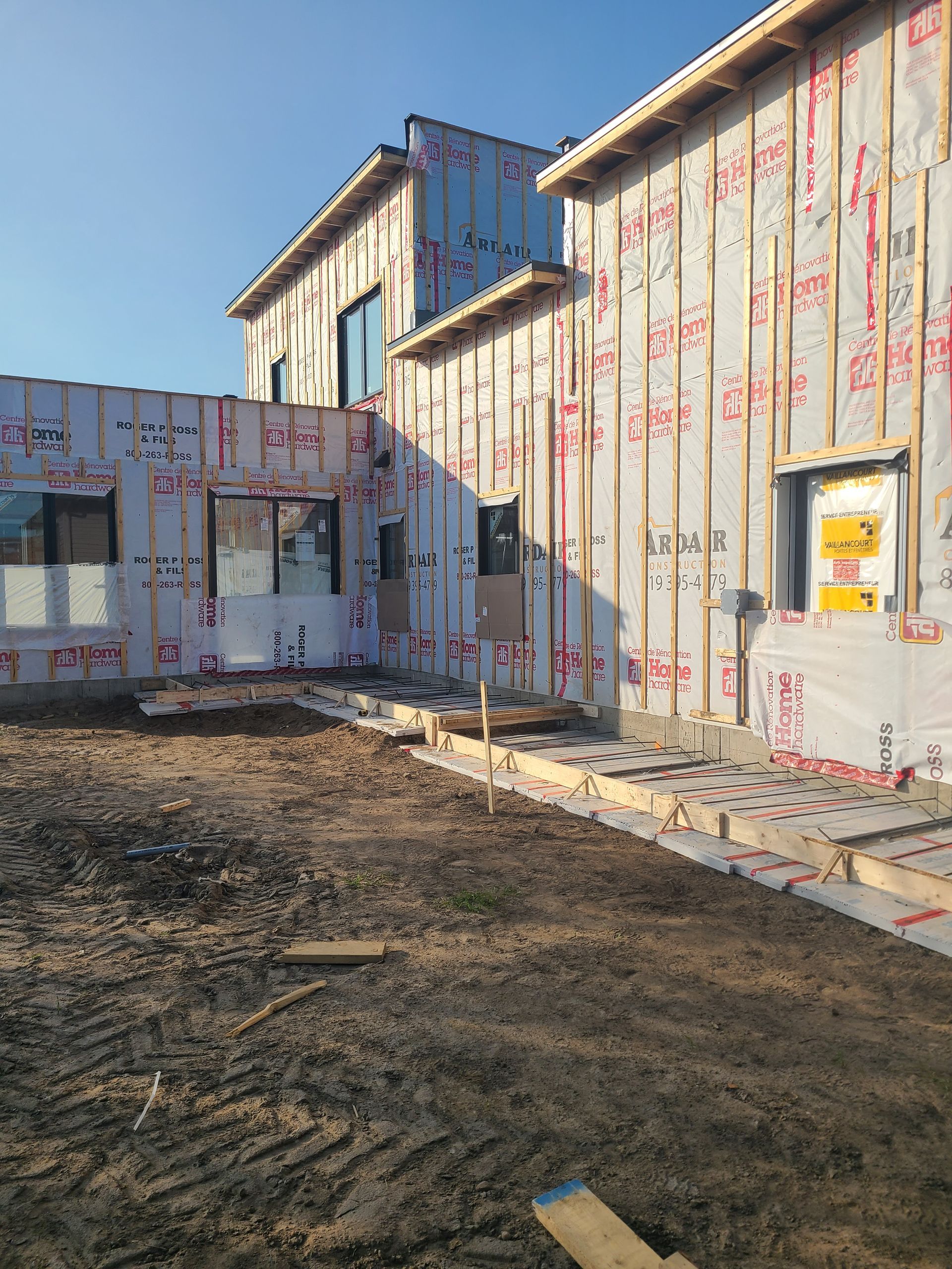 Un immeuble résidentiel à plusieurs niveaux en construction, dont les murs extérieurs sont recouverts de bâches de protection blanches.