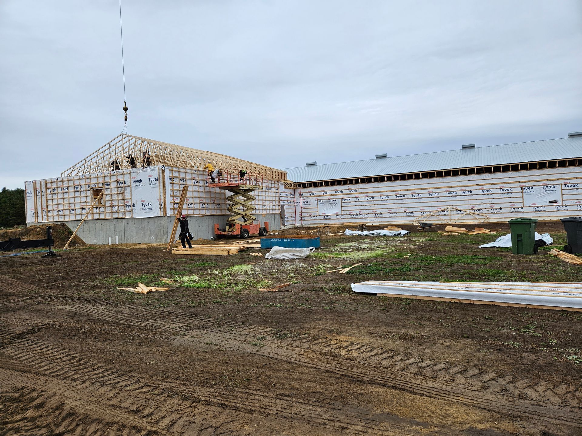 Des ouvriers du bâtiment construisent une structure à ossature bois sur des fondations en béton, sur un terrain boueux en plein air.