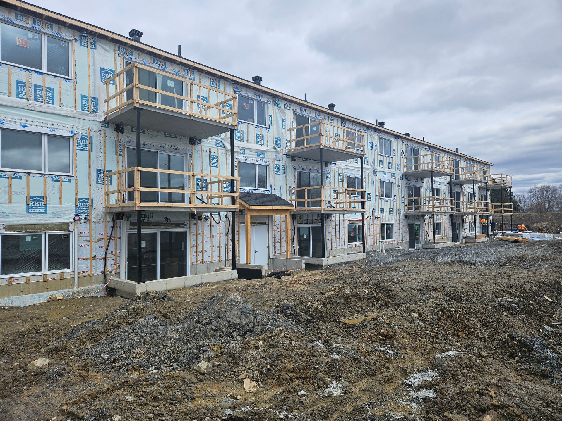 Un immeuble d'appartements de plusieurs étages en construction, inachevé, avec un revêtement extérieur de couleur claire et des balcons en bois.