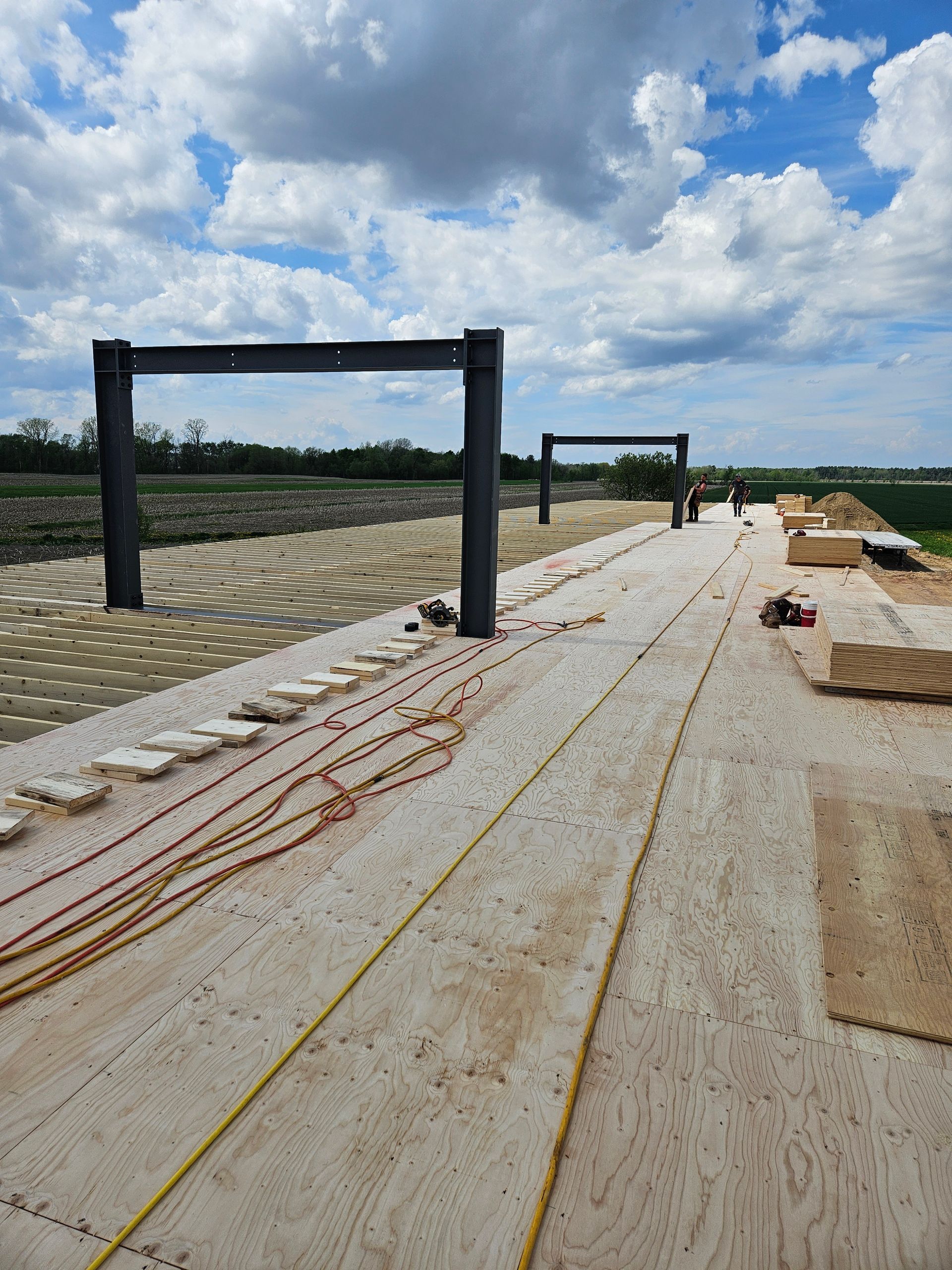 Chantier de construction avec deux structures d'arches en acier sur un sol en gravier, présentant un chemin circulaire partiellement construit.